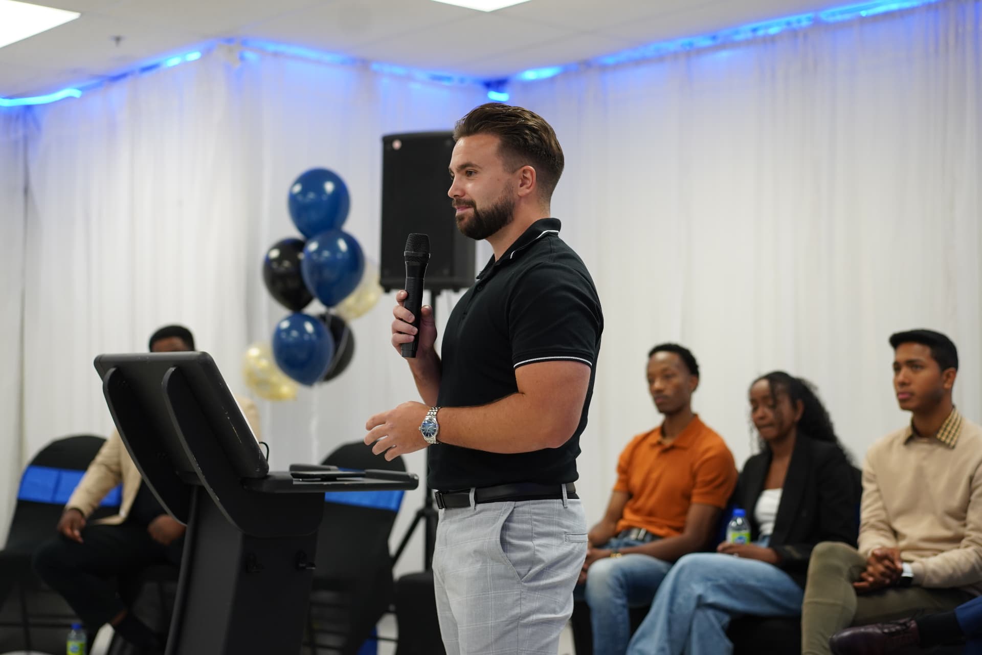 Shayne speaking on stage at an event with a seated audience behind him